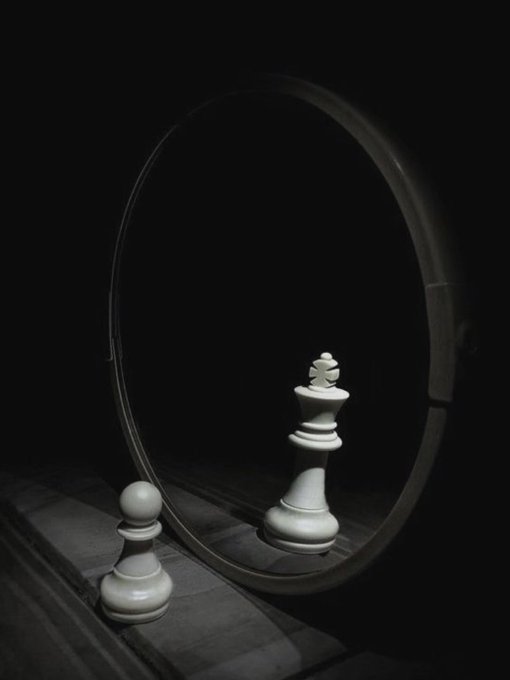 A black and white photograph of a chess king piece reflected in a mirror, creating an interesting visual effect on a chessboard.
