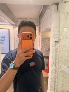 A mirror selfie of a man wearing a dark blue work shirt and an orange iPhone, with his face obscured by the phone.