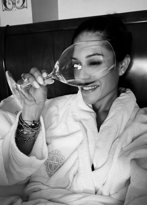 A woman wearing a plush bathrobe with an embroidered crest smiles while sipping from a wine glass, capturing a luxurious moment at the Principe di Savoia hotel in Milan for a "good night, good night."