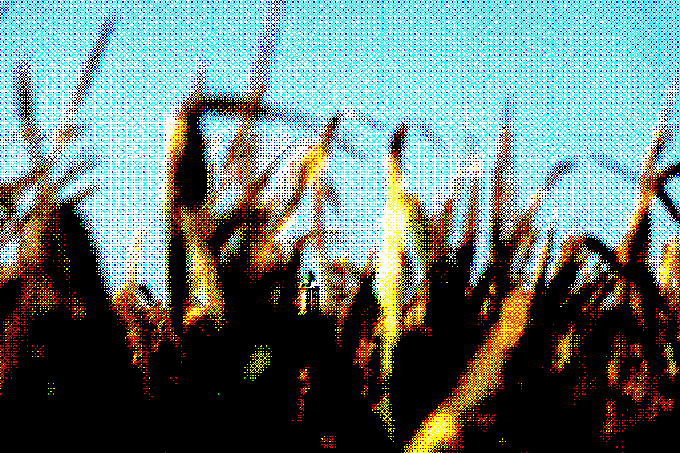A heavily pixelated image shows a crowd with raised hands in front of a structure against a bright blue sky.
