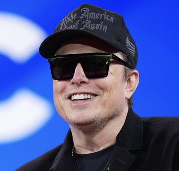 A close-up photo of Elon Musk smiling, wearing a 'Make America Based Again' cap and dark sunglasses.