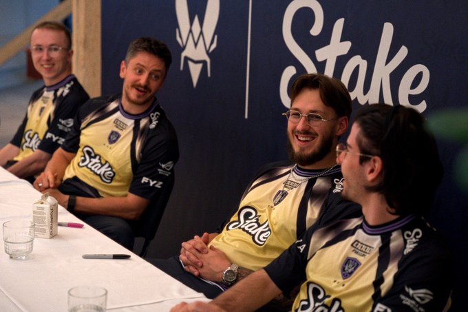 Members of Team Vitality, wearing their yellow and black jerseys featuring the "Stake" sponsor logo, sit at a table for an autograph session ahead of the BLAST Porto tournament.
