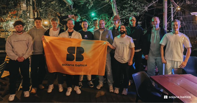 A group of young men pose together at night holding an orange flag with the "SB solana baltics" logo, appearing to be members of the Solana Baltics community. The image visually supports the post's declaration of switching allegiance from Bitcoin to Solana, showcasing a gathering of Solana enthusiasts celebrating their crypto community.