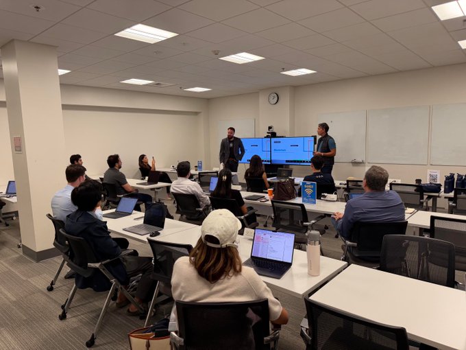 UCLA Anderson students attend the first Cardano masterclass, working on laptops and presenting Web3 business ideas pitched using AI-assisted smart contract development. The classroom scene reflects the university partnership’s focus on educating the next generation of blockchain builders.