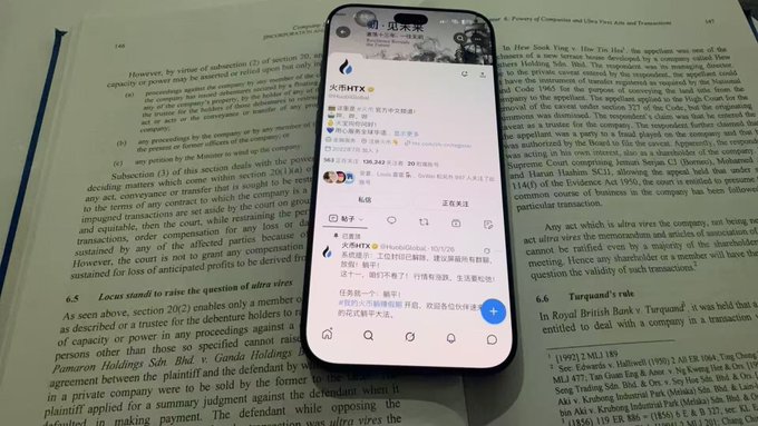 A smartphone displaying a social media feed with Chinese text and a 'HiBTX' logo rests on top of an open legal textbook discussing company law and share transfers.