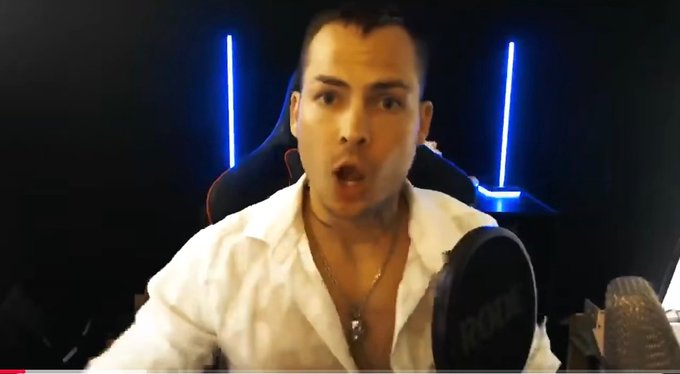 A man in an unbuttoned white shirt speaking into a Rode microphone with a shocked expression, seated in front of blue neon lights.