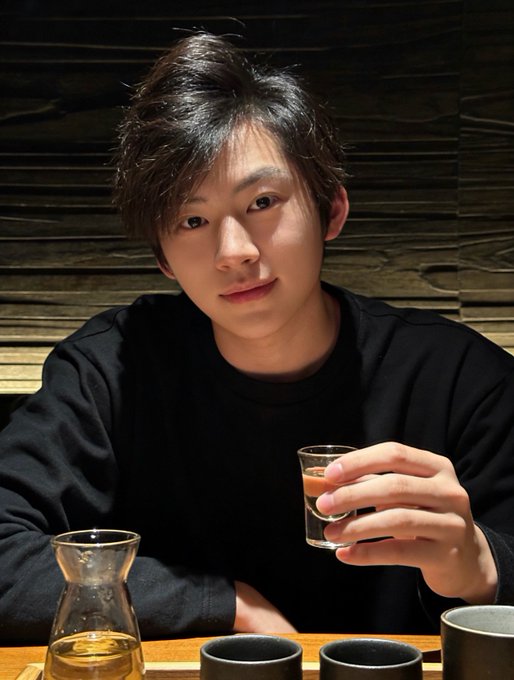 A young man with styled dark hair, wearing a black sweater, sits at a wooden table holding a small glass of clear liquor, with a traditional Japanese sake carafe and ceramic cups arranged in front of him against a dark wood-paneled wall.

The image evokes the post's message about stepping away from trading screens, shifting focus to real life, and enjoying mindful social moments—with the candid, relaxed portrait mirroring the call to disengage from losing trades and engage with the present.