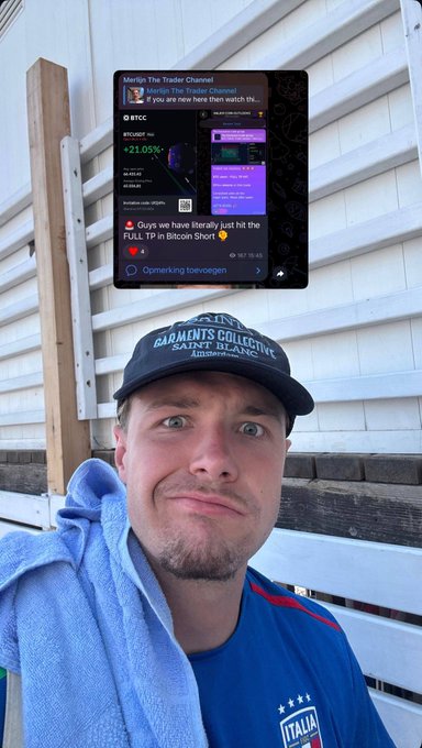 A man wearing a "Garments Collective Saint Blanc" cap and an Italy hoodie makes an exaggerated, excited facial expression while showing a phone screen displaying a "+21.05%" gain from $BTCC and a Telegram notification reading "Ogyq we have literally just hit the FULL TP in Bitcoin Short." The image visually reinforces the post's claim about receiving a full take-profit notification while going about his day.