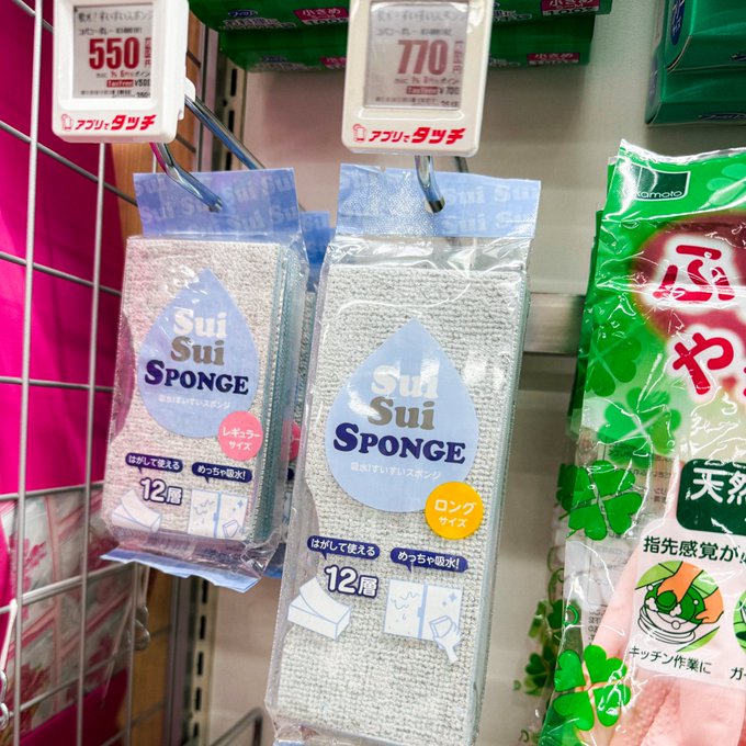 Two "Sui Sui Sponge" packages (12-count) hang on a store shelf, priced at ¥550 for the smaller "レギュラーサイズ" (regular size) and ¥770 for the larger "ロングサイズ" (long size), alongside a green Kameyama sponge product, perfectly illustrating the playful pun post about "Sui" holders crying and needing tear-soaking sponges.