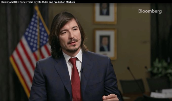 A Bloomberg interview screenshot showing Vlad Tenev, CEO of Robinhood, in a navy suit and red tie, with the headline 'Robinhood CEO Tenev Talks Crypto Rules and Prediction Markets.'