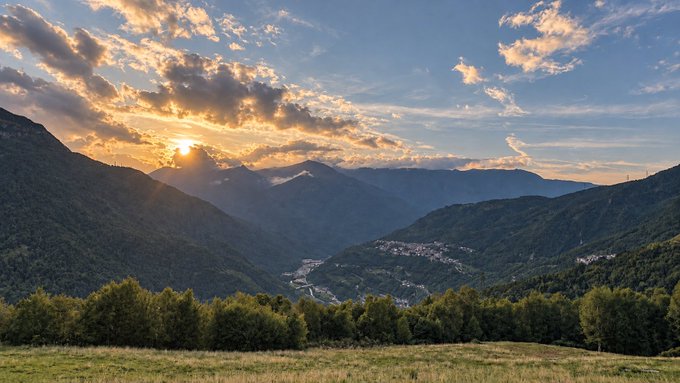 A breathtaking sunset casts golden light over a lush mountain valley, where a small town nestles along a winding river surrounded by rolling, tree-covered peaks. The serene landscape mirrors the post's calm, reflective tone—encouraging patience and a measured approach, much like watching the sun set slowly before planning the next move.
