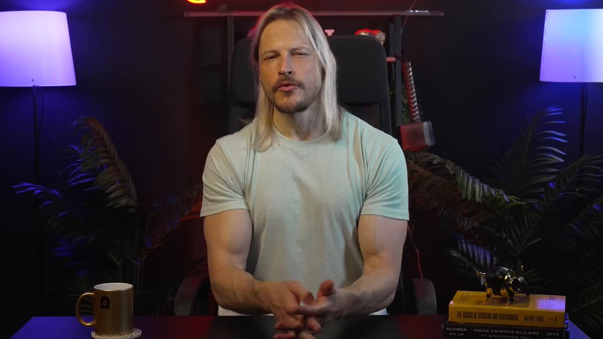The image shows a man sitting behind a desk with his hands folded, wearing a white t-shirt. There are two lamps in front of him - one blue and one purple. The background features a black wall with a plant placed on top of it. The text "Binance just made tokenised stocks real for 240 million users. Not a whitepaper. Not a testnet. Not a roadmap promise. Live. Right now. On Binance Alpha. NVDAon. TSLAon. GOOGLon. AAPLon. Real Nvidia. Real Tesla. Backed 1:1 by the actual securities held at".