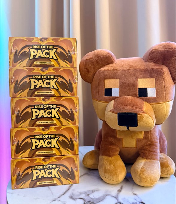 Five stacked boxes of 'Rise of the Pack' booster packs next to a brown and yellow Minecraft-styled bear plush toy.