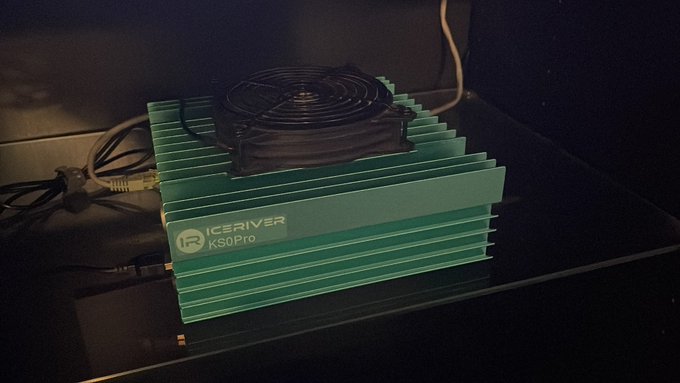 A green ICERIVER KS0Pro crypto mining rig sits on a shelf with a cooling fan visible on top, powering support for the $KAS Kaspa network.
