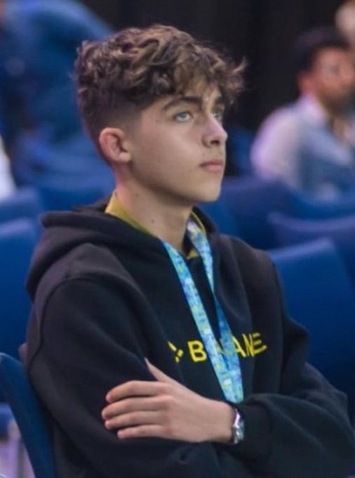 A 19-year-old crypto trader wearing a black hoodie with partial text reading "BYB" or "BYBI" visible across the chest, along with a blue lanyard, sits with crossed arms looking thoughtfully to the side—illustrating the post's point about how trading in crypto over the past five years has aged him far beyond his years.