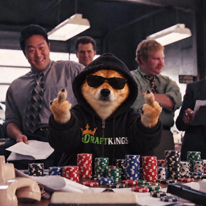 A digital artwork of a Shiba Inu dog wearing sunglasses and a black DraftKings hoodie, sitting at a poker table with stacks of chips while office workers watch in the background.