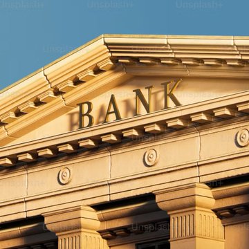 The image shows the upper facade of a classical-style building featuring the word "BANK" in prominent gold lettering against a stone pediment, with rosette details and architectural molding beneath a clear blue sky. This traditional bank imagery visually reinforces the post's message about the growing convergence between crypto and traditional finance, symbolizing the legitimacy and institutional credibility that established financial architecture represents in the new digital asset landscape.