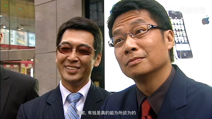Two men in business suits pose together, one wearing a pinstripe suit with a striped tie and tinted glasses smiling, while the other wears a dark suit with a red tie, with Chinese subtitles visible at the bottom of the frame. The image appears unrelated to the post about the EU sanctioning HTX Exchange.
