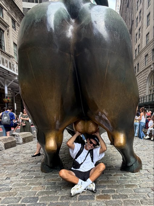A tourist poses underneath the rear end of the Charging Bull statue in New York City.