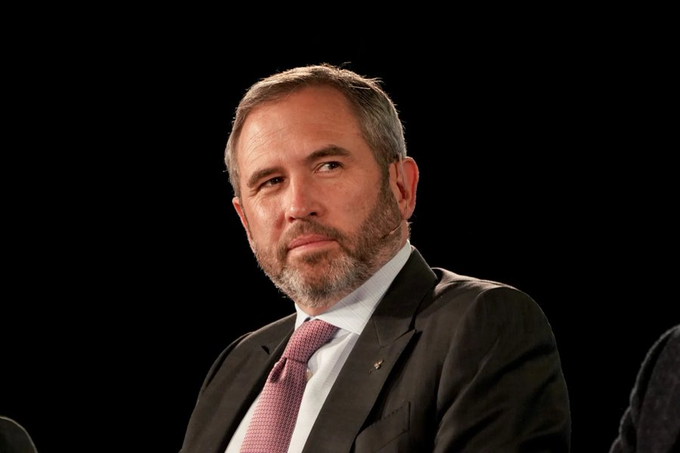 A man with a beard, wearing a dark suit and a pink patterned tie, sits against a black background during what appears to be a formal speaking event or interview. Given the post's context about Ripple and XRP, this is likely Brad Garlinghouse, CEO of Ripple, discussing the company's strategic shift following its legal battles over XRP's classification.