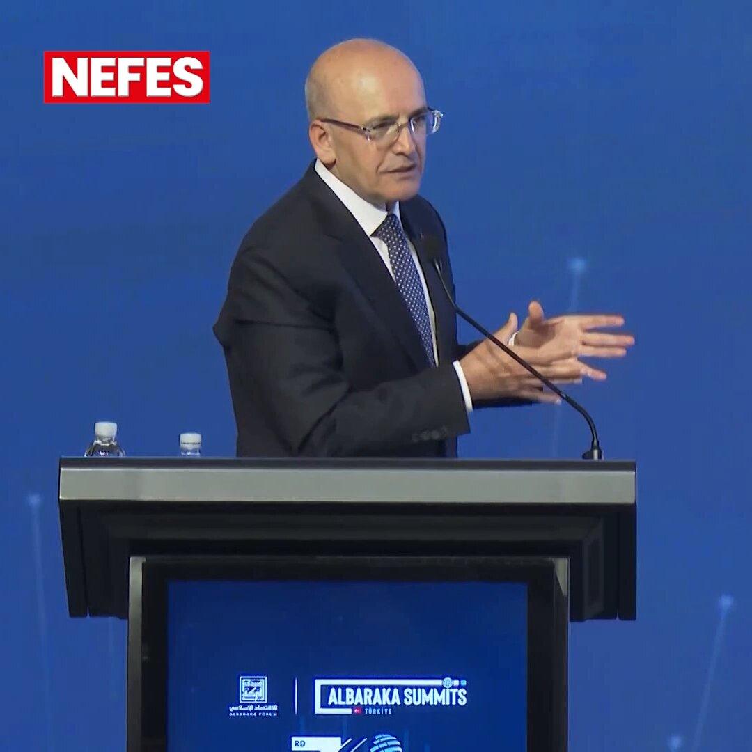 The image features a man standing at a podium with his hands outstretched, giving a speech or presentation. The background of the image shows a blue wall, which could be part of an event or conference setting. There are also two TVs visible in the scene - one is located behind the speaker and another on the right side of the image.

The post includes text that reads "Nefes" and "Albarakat Summits", possibly indicating a connection between the event and the summit. The man at the podium appears to be addressing an audience, as he has his hands outstretched in front of him.