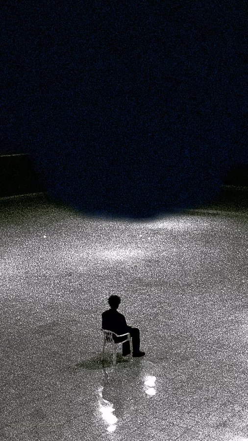 A solitary silhouetted figure sits on a chair in a vast, glittering silver expanse under a dark sky, with light reflecting on the ground around them.