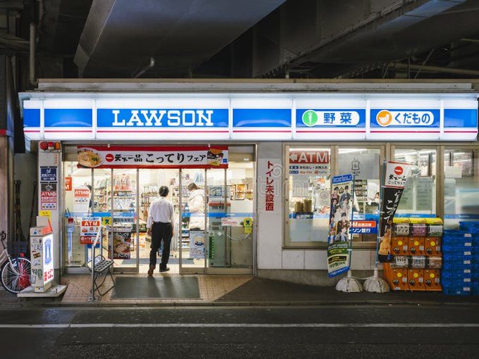 A nighttime view of a Lawson convenience store in Japan, displaying its blue "LAWSON" sign, ATM services, and Japanese text for vegetables ("野菜") and medicines ("薬"), with a customer standing at the entrance. The image visually connects to the announcement of Lawson launching a stablecoin remittance service in partnership with Digital Garage and Circle.