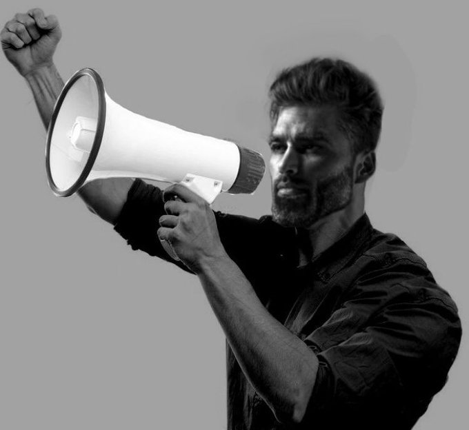 A determined bearded man raises a megaphone to his mouth while pumping his fist in the air, channeling the triumphant energy of the "ITS BUNDLED!!" announcement.