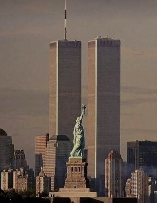 A surreal scene featuring the Statue of Liberty positioned directly between the Twin Towers of the World Trade Center against a hazy sky.