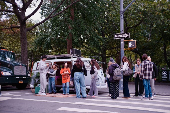 A group of stylish young people gather at a city crosswalk near a van, with a "ONE WAY" sign visible overhead, capturing the kind of real-life social encounter the post highlights through AnumaAI's private memory profiles starting in NYC.