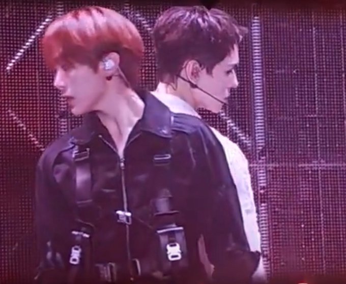 The image features two young men wearing black outfits, with one of them having red hair. They are standing close together against a purple background, which appears to be a stage or concert venue. The photo has been edited to include text that reads "not to be a solboist but omg the iconic trigger to gemini transition was done by seungkwan and vernon ?". This suggests that they might have performed at a concert where the iconic "gemini" transition was used as part of their performance.