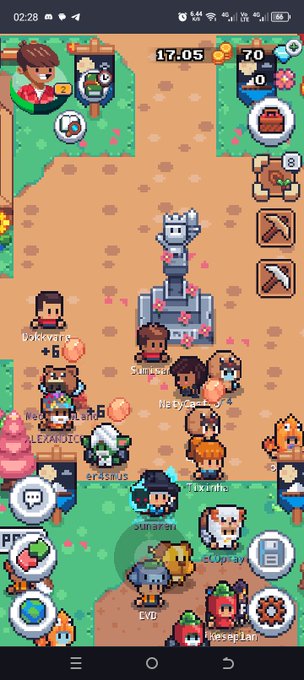 A pixel-art mobile game screenshot showing a village scene with various player characters gathered around a central statue, with usernames and game UI elements visible.