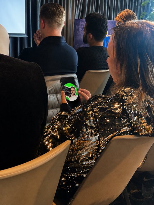 A woman in a sequined jacket sits in a conference audience holding up her phone, which displays a FaceTime-style screen showing the name "Richard Heart" alongside a photo of a bearded man. The image visually ties into the post's bullish sentiment about PulseChain by showing the project's controversial founder, whose endorsements often drive the coin's price movements.