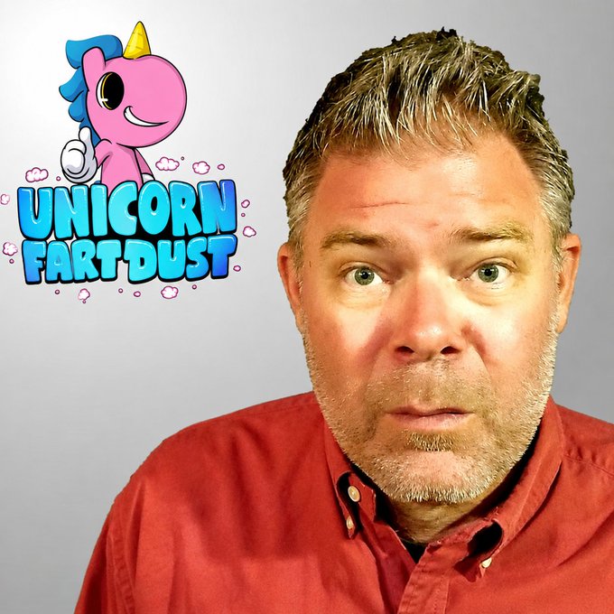 A close-up of a middle-aged man with short grey hair and stubble wearing a red shirt, positioned next to a cartoonish logo that reads 'UNICORN FART DUST' featuring a pink unicorn blowing bubbles.
