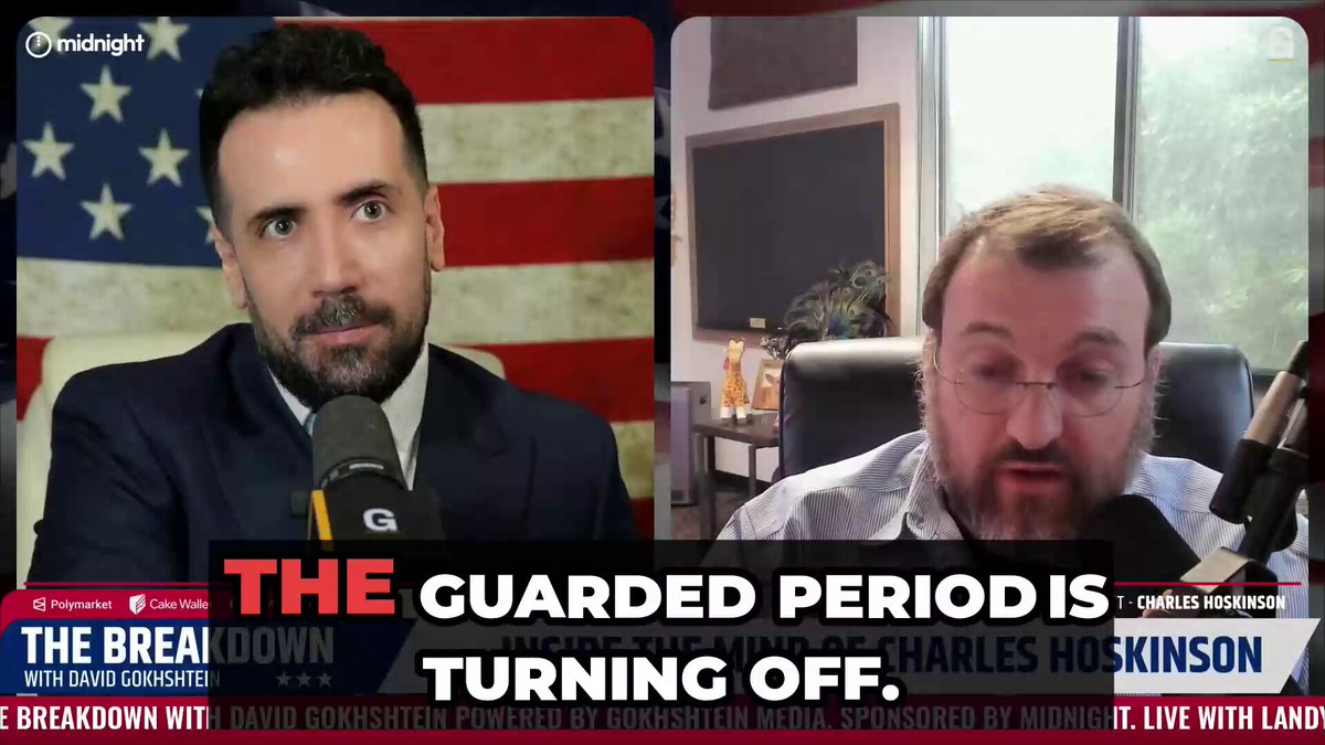 The image shows a man wearing glasses sitting behind a microphone during an interview, while another person is also present in the scene. The background features an American flag, which suggests that this might be taking place in the United States. The text on the image reads "The guarded period is coming to an end as the network prepares for its next hard fork, unlocking major upgrades." This implies that the interview is related to a political or financial event and could be discussing the transition from one governing period to another.