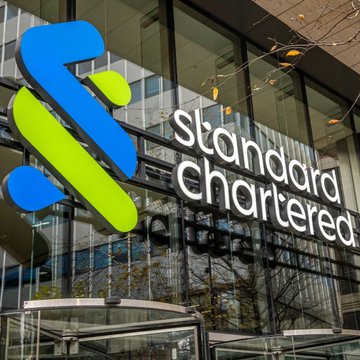 A glass-fronted building displays the prominent blue and green logo and "Standard Chartered" signage of the global bank, visually connecting the institution to its newly announced coverage initiation on Chainlink with ambitious price targets of $13 by year-end and $200 by 2030.