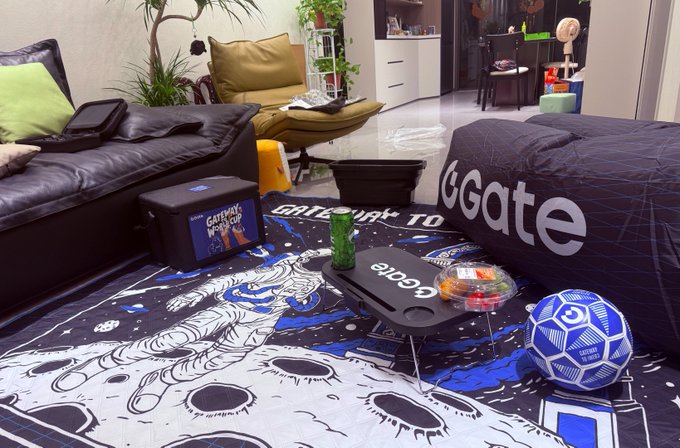 A cozy gaming setup in a living room includes a 'GATEWAY' blanket, a blue and white patterned rug, a bean bag chair labeled 'GGate', a Gateway Workshop cooler, and a blue soccer ball.