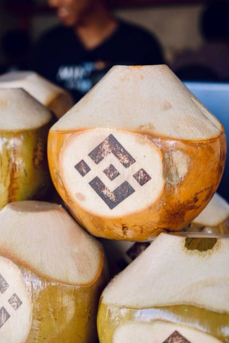A close-up shot showcases a stack of young, peeled coconuts, prominently featuring the Binance logo branded on their surface. The image ties into the "GM" (Good Morning) theme, offering a tropical and refreshing vibe perfect for a crypto enthusiast's morning greeting.