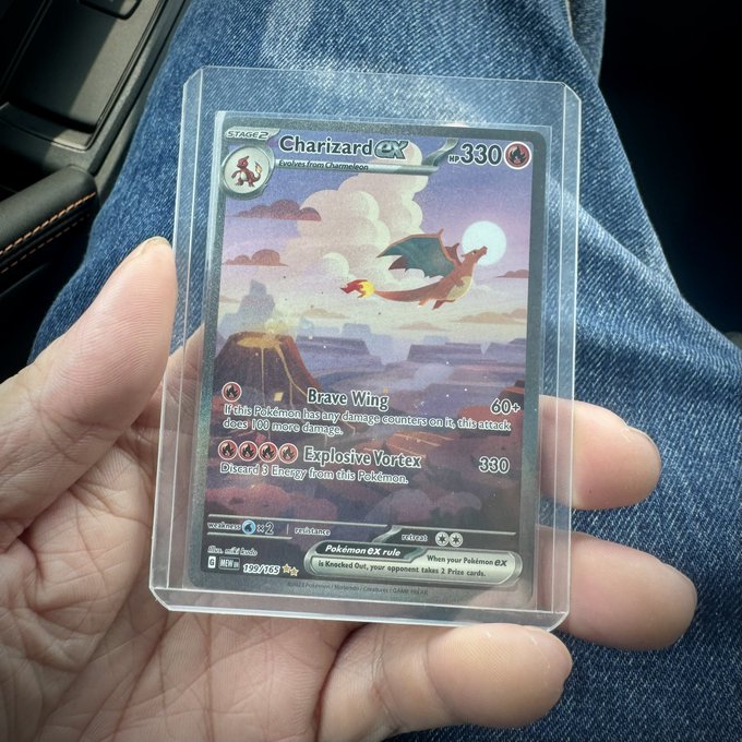 A hand holds a holographic Charizard ex Pokémon trading card (HP 330) featuring "Brave Wing" and "Explosive Vortex" attacks, encased in a protective sleeve.