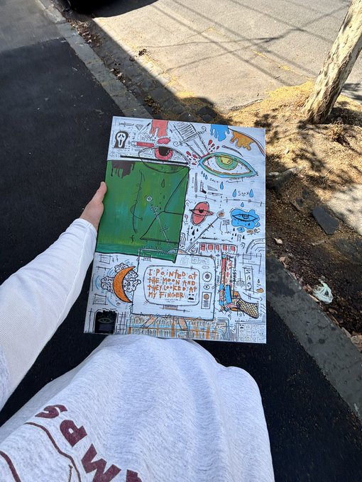 A hand-drawn poster with colorful doodles and the text 'I PAINTED AT THE MENTAL HEALTH FACILITIES IN MY FINGER' held outdoors on a sunny day.