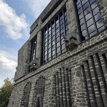A low-angle view of a stone building with large multi-paned windows set against a blue sky with scattered clouds.