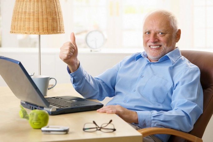 An older man with a white beard in a blue shirt sits at a desk with a laptop, giving a thumbs-up while smiling, with a green apple and reading glasses on the table. The image humorously represents the forced optimism of a MEV bot operator whose token gains are shrinking in actual dollar value, mirroring Jaredfromsubway.eth's situation.