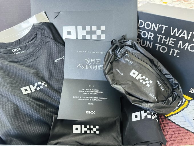 An unboxing of OKX running gear merchandise including a black shirt, belt bag, shorts, and a card with Chinese text reading '等月圆不如问月雨' for a Happy Mid-Autumn Test.