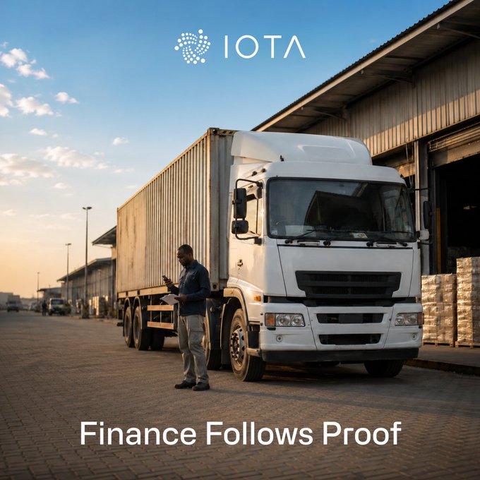 A promotional image for IOTA featuring a man holding a tablet next to a large white semi-truck parked outside a warehouse, with the tagline 'Finance Follows Proof' at the bottom.