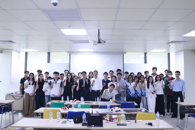 A group of students and faculty pose together in a modern classroom at UEF University, smiling and making thumbs-up gestures after a meetup. The setting and the post about Cardano Ambassador Ha Nguyen's event recap on decentralized funding models for student founders align with the image, capturing the participants of the discussion comparing traditional venture capital with decentralized financing options.