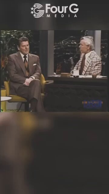 The image shows two men sitting at a desk, with one man wearing a suit and tie while the other has a beard. The background of the image features a sign that says "Four G Media" along with an image of a microphone on top of the desk.