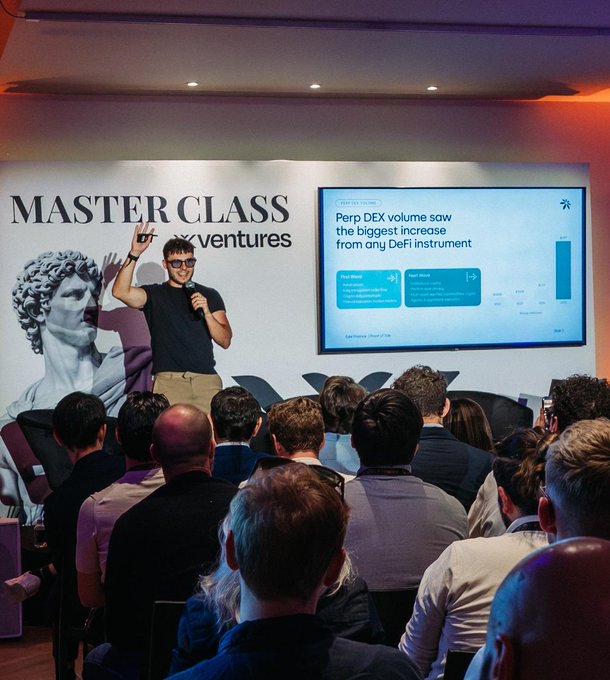 The image shows a man standing at a podium, giving a presentation or speech to an audience of people sitting behind him. There are several individuals seated in chairs around the room, attentively listening to the speaker. The setting appears to be a conference or event space with a large screen displaying information related to the presentation. The post on social media mentions that the event took place at the airport while Edel is among the fastest-growing apps on @CantonNetwork.