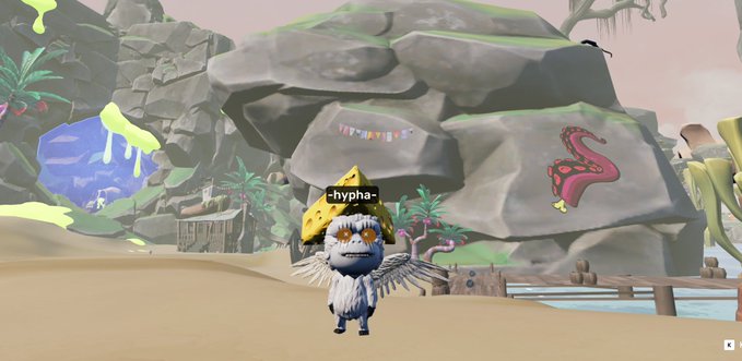 A screenshot from a video game featuring a character named '-hypha-' wearing a yellow cheese hat, standing in a rocky, tropical-themed environment with a pink flamingo drawing on a rock.
