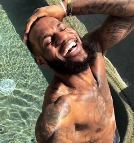A shirtless, smiling bearded man with extensive tattoos poses joyfully in a pool, arms behind his head, capturing a carefree moment. The image, paired with the post "97 UNITED STATES DOLLARS PER COIN," evokes a lifestyle of financial success and leisure, suggesting the cost of a coin tied to this kind of luxurious, upbeat vibe.