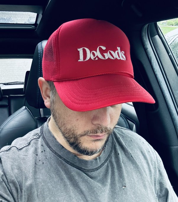 A man wearing a red "DeGods" trucker cap sits in a car, head tilted down, paired with a "Good Saturday morning, Solana summer in progress" post celebrating the DeGods NFT community on the Solana blockchain.
